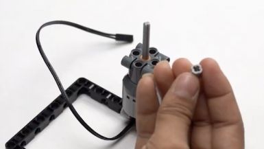 Take a full bush and place it onto the axle to secure the components in the DIY hoop game bot, promoting robotics skills development and creative play.