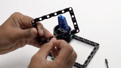 Attach two pegs to an 11 by 7 block and secure it in place. This construction is part of building the mobile holder for your Object Finder Robot, which will utilize advanced AI recognition.