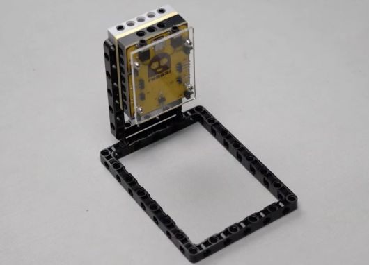 Bring the Roboki microcontroller and firmly attach it onto the brick, ensuring proper alignment to enhance the Entry Guard bot, a practical project in STEM robotics that emphasizes sensor applications, automated traffic monitoring, and hands-on learning for robotics enthusiasts.