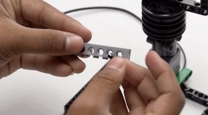 Connect two pegs to a 1 by 6 brick with holes and attach it to the 15 by 11 block. This assembly is vital for the stability of the Object Finder Robot, enhancing its structure for advanced functionality.